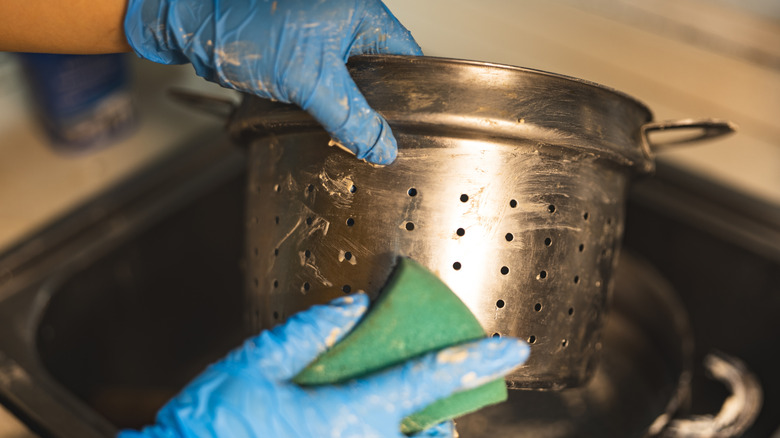 someone with blue gloves cleaning a steel pot