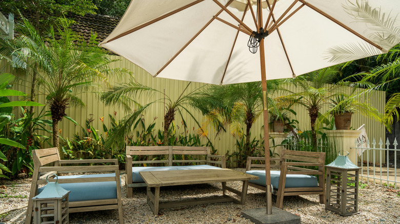 A gravel patio with table and chairs, and shade provided by an umbrella