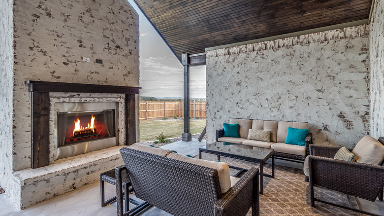 A covered patio area with a large fireplace, chimney, and comfortable seating