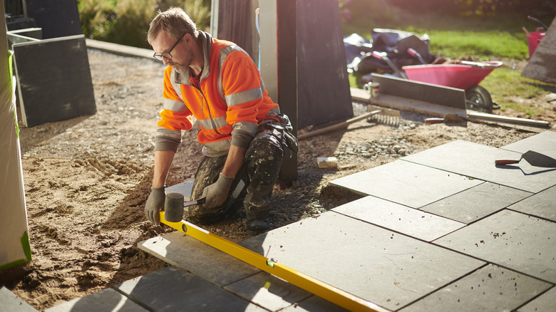 A worker laying a patio, using a spirit level to ensure a proper slope for drainage