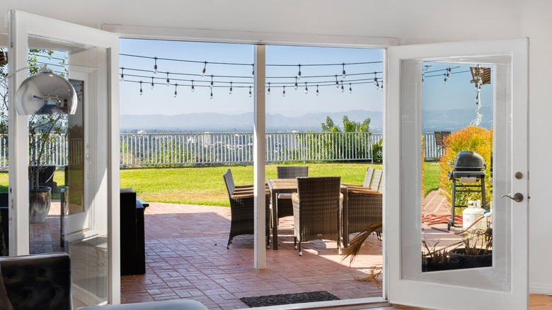 A shot from a living room, looking out onto a patio with table and chairs and a beautiful view beyond
