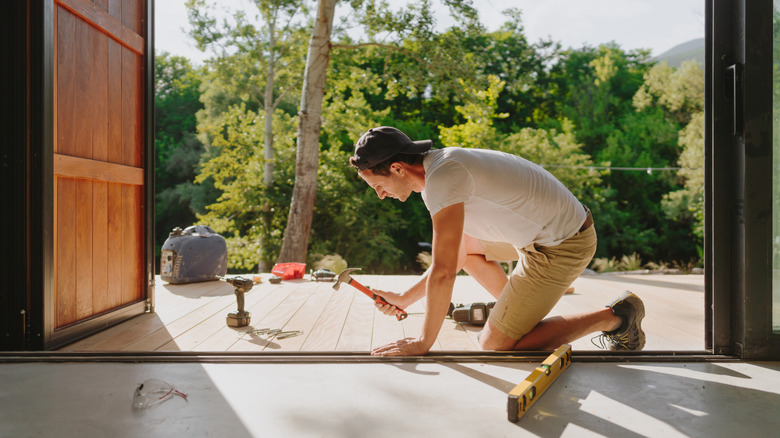 Person hammering decking boards with trees in background.
