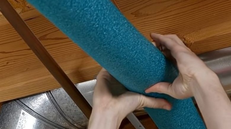 Hands placing pool noodle over exposed copper pipes