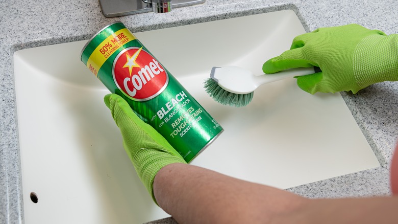 A person scrubs a bathroom sink with Comet.