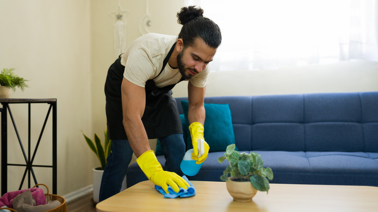 A man cleaning a table with a spray and a sponge.