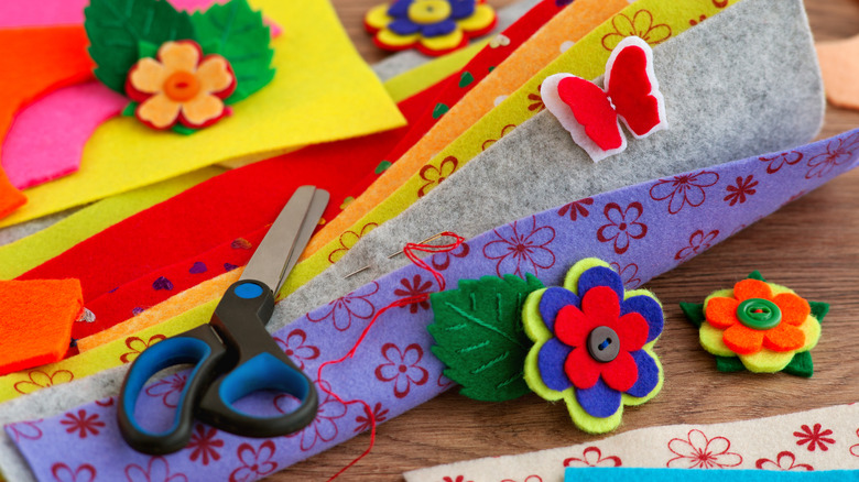 Colorful felt sheets arranged on a wooden desktop with other craft supplies and tools.