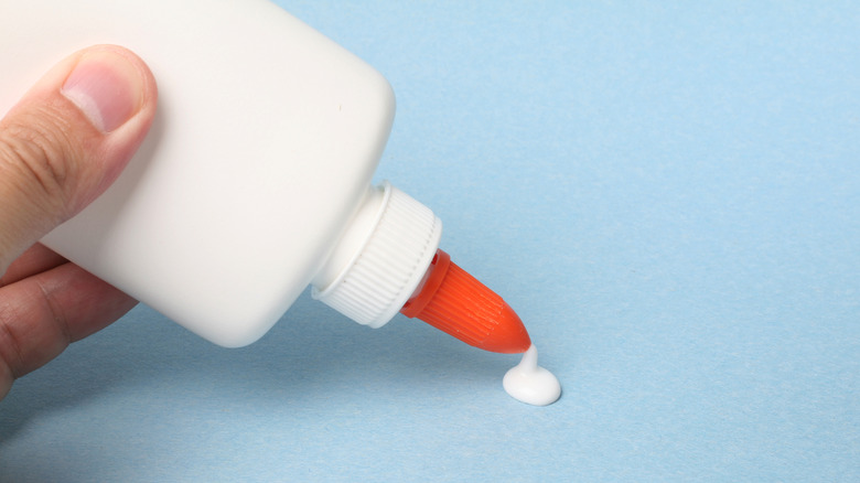 A hand squeezes craft glue onto a piece of light blue paper.