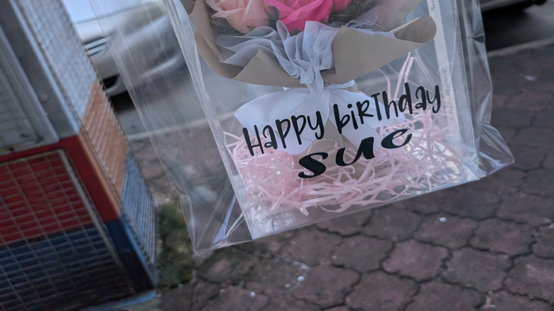 A homemade craft inside a gift bag with ribbons and a happy birthday sign.