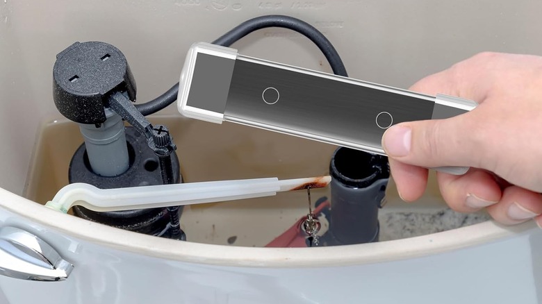 A person about to insert a magnetic cleaner in their toilet tank