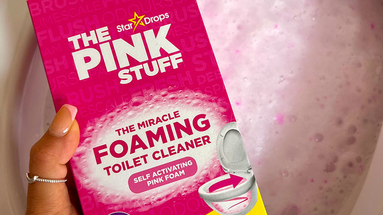 A woman holding a box of The Pink Stuff while her toilet foams in the background