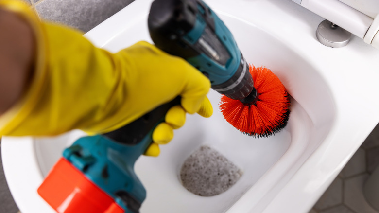 A person using a drill with a brush attachment to clean a toilet