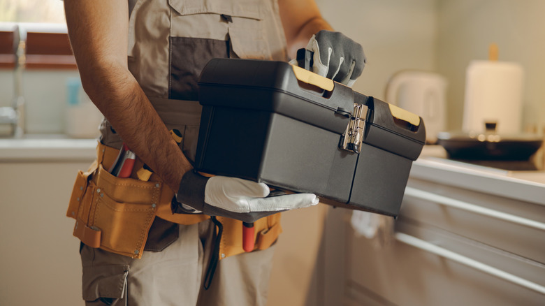 A person holidng a toolbox in the kitchen
