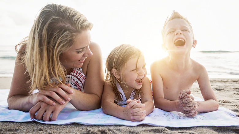 a mother, daughter, and son laying on a blanket at the beach