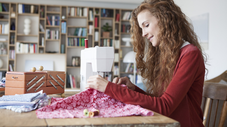woman sewing a pink and red patterned fabric with other fabric next to her
