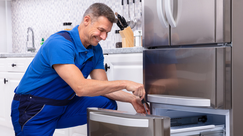 A man servicing a refrigerator in a kitchen