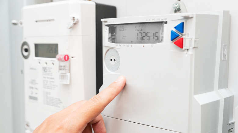 A hand and finger pointing at numbers on a home's electric meter