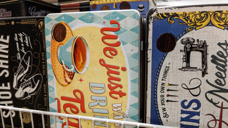 close up of three vintage tea, sewing needles, and shoe polish tins on wire rack