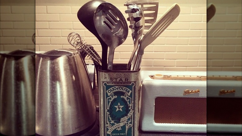 vintage olive oil tin being used to holding cooking utensils on counter