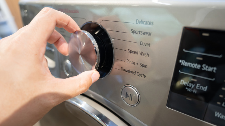A hand adjusts the dial of a silver washing machine