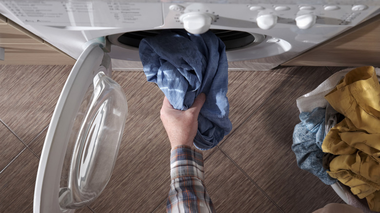 Top-down view of a hand pushing dirty clothes into a washing machine