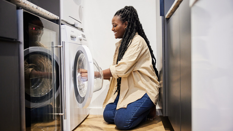 A smiling woman loads a washing machine with clothes