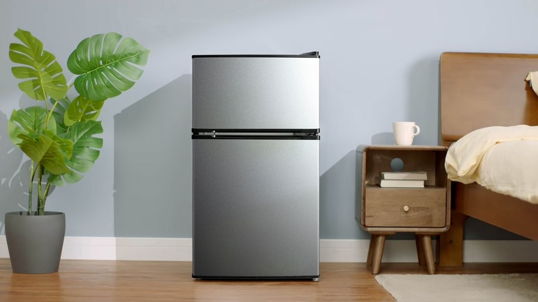 A small two-door stainless steel refrigerator in a bedroom
