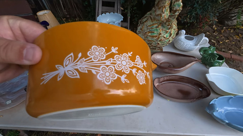Person holding orange Pyrex dish in front of flea market table