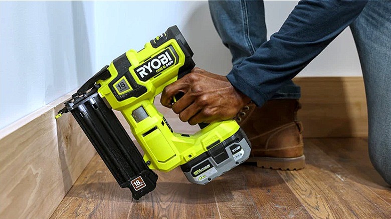 Someone using a brad nailer to install baseboards