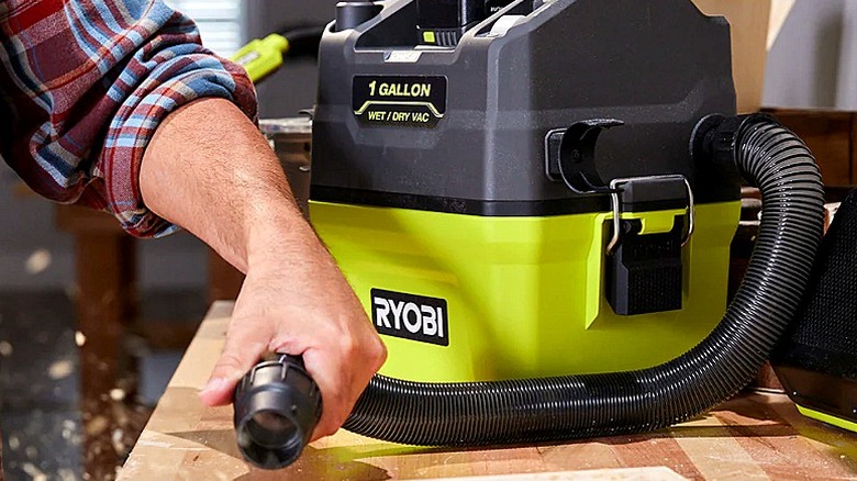 Someone using a wet/dry vacuum to clean a table
