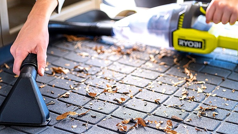 Someone using a handheld vacuum to suck up leaves in a car trunk