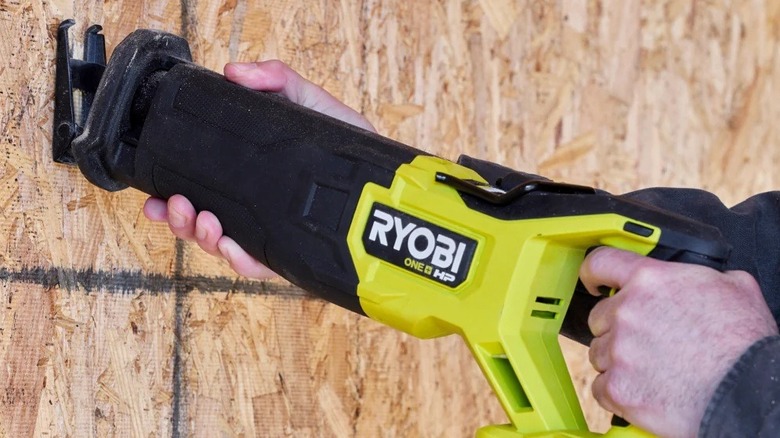Person cutting through plywood with a Ryobi reciprocating saw
