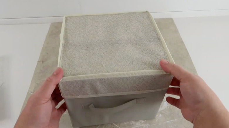 Person's hand's putting a handmade fabric lid on a storage fabric storage cube.