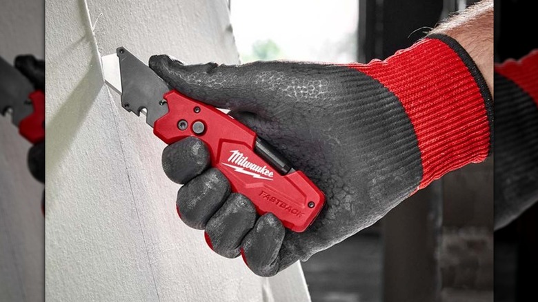 A person scoring drywall with Milwaukee's FASTBACK 6-in-1 Folding Utility Knife