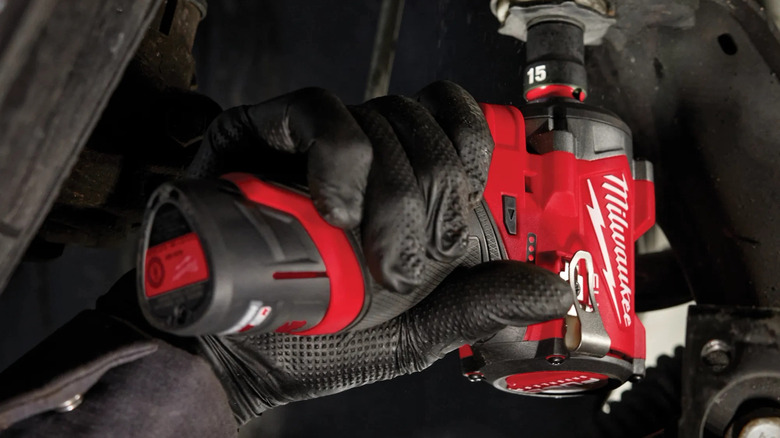 Close-up of a person using Milwaukee's M12 FUEL 12V Lithium-Ion Brushless Cordless Stubby ½-inch Impact Wrench on a fastener under a vehicle