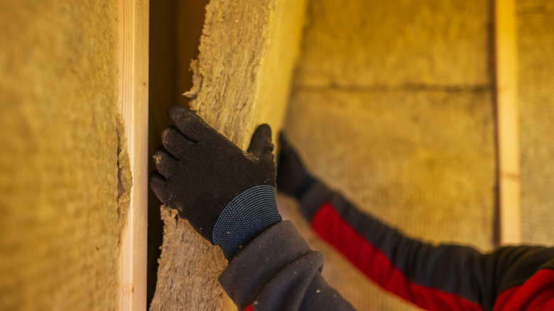 Close-up of a person installing mineral wool insulation in a shed wall