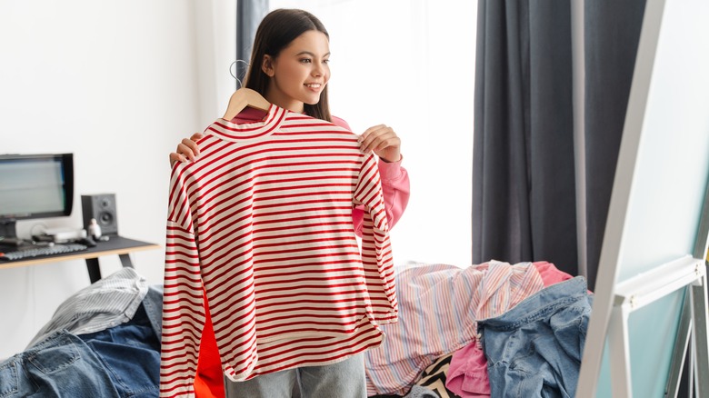A person holding up a shirt to look in the mirror