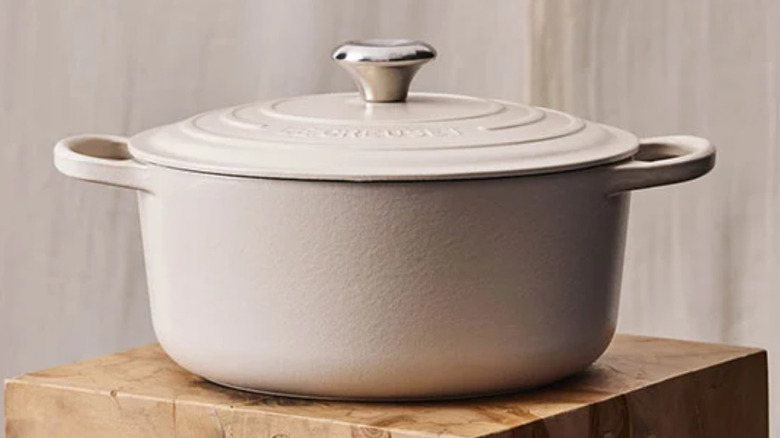 A creme colored Le Creuset Dutch oven on a wooden stool
