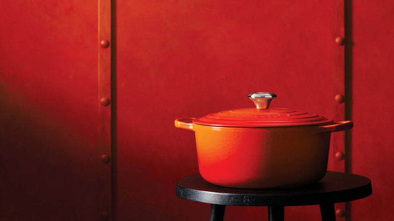 A bright orange Le Creuset Dutch oven in front of a red wall.