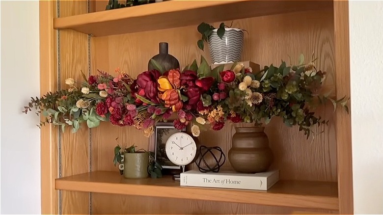 A fall-themed garland DIY project on a bookshelf made with fake flowers