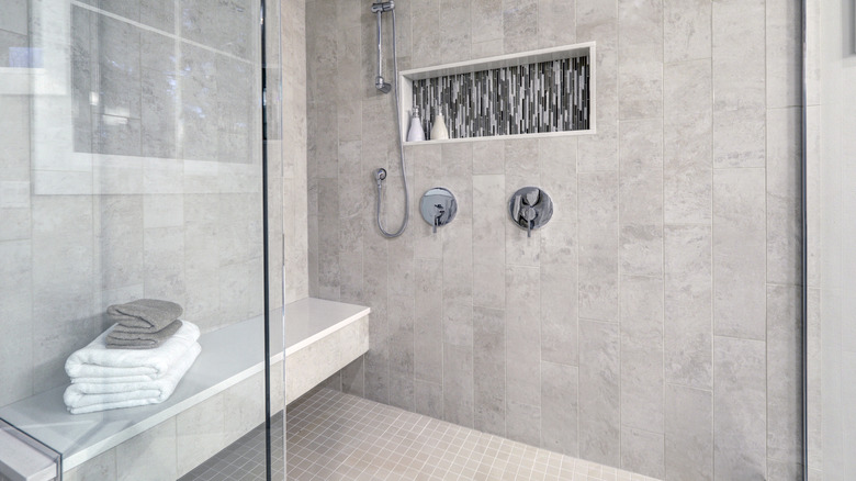 Glass walk-in shower with gray subway tiled surround accented with mosaic tile strip in wall niche of brand new home bathroom.