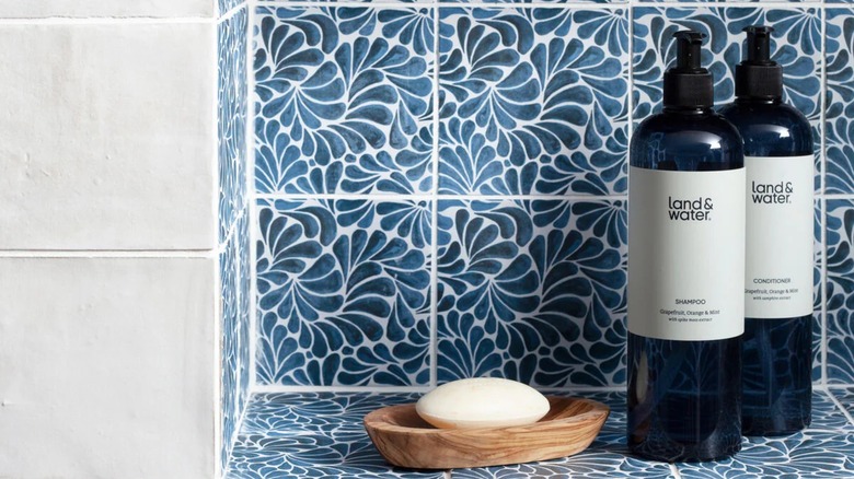 Beautiful blue and white tiles in shower nook with soap and containers of shampoo and conditioner.