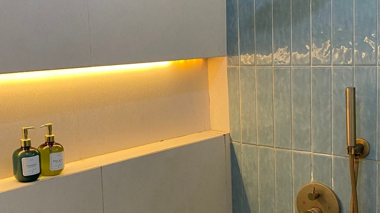 Modern Minimalist Shower Interior with Brass Fixtures, Blue Wall Tiles, and LED Shelf Lighting in a Cozy Bathroom Setting. Jogja, Indonesia, May 25, 2025