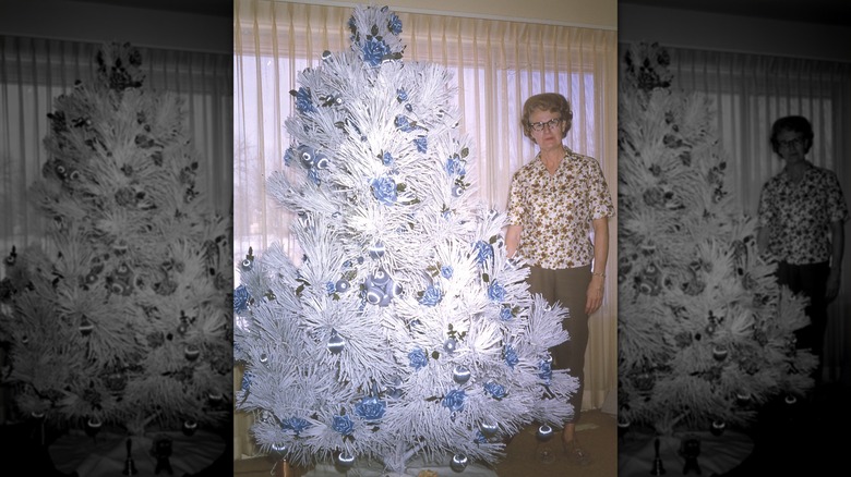 A woman stands proudly beside her white flocked Christmas tree with white and blue baubles