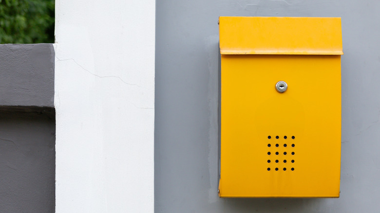 A yellow mailbox on a gray wall