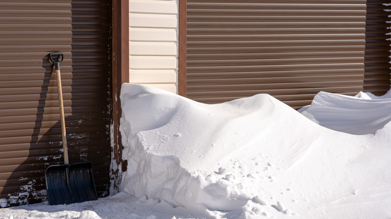 snow piled outside of a house with a shovel