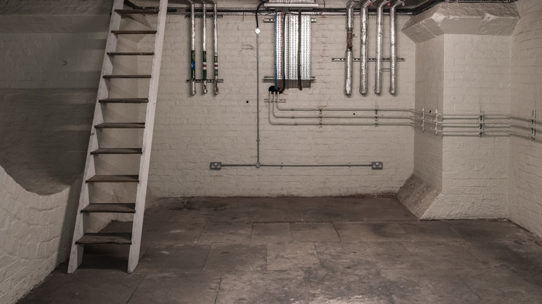 An empty basement contains stairs and plumbing pipes