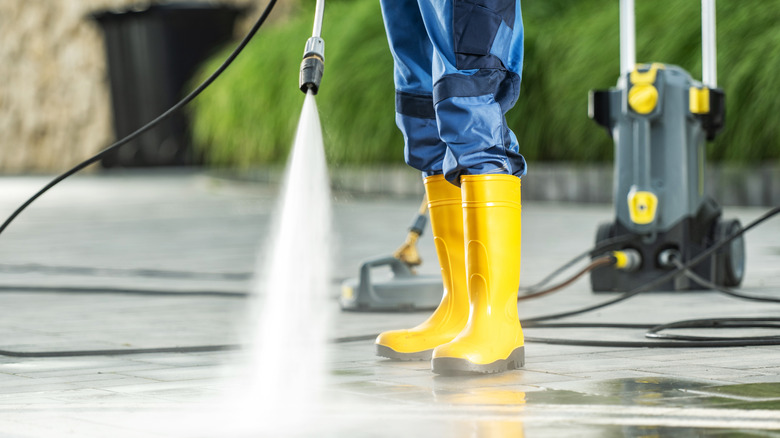 Person powerwashing driveway in rubber boots