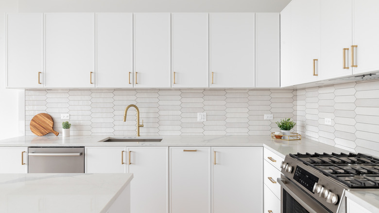 An all-white kitchen with gold accents and a horizontal elongated hexagon tile backsplash.