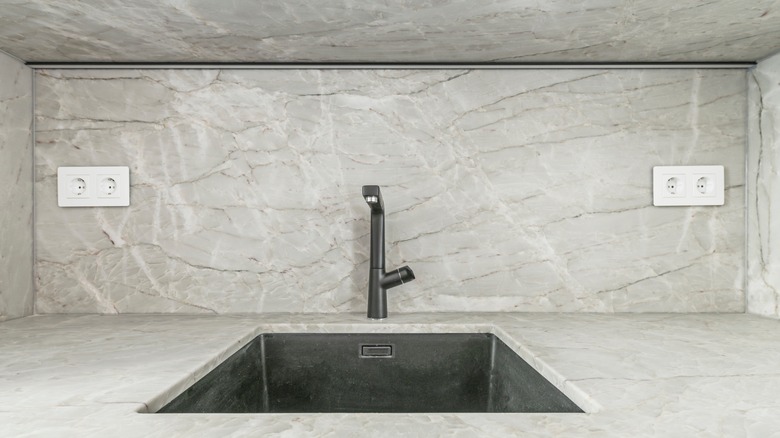 A gray and gold-veined marble slab backsplash in a kitchen.