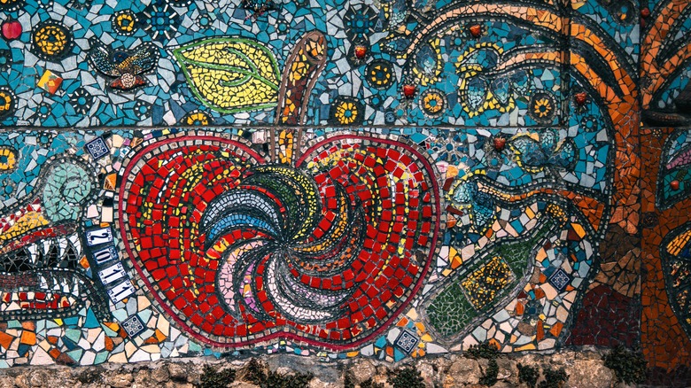 A mosaic mural of a tree and an apple on a kitchen backsplash.